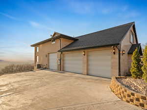 View of side of property with roof with shingles, concrete driveway, and a garage