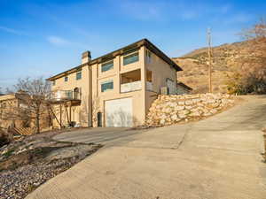 West View of front facade featuring a balcony, stucco siding, driveway, a garage, and a chimney