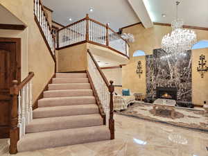 Entrance: Stairs with a towering ceiling, beamed ceiling, a high end fireplace, marble tiled flooring, and a chandelier