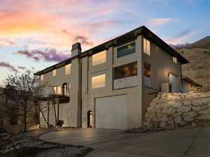 View of front of home featuring a balcony, driveway, a chimney, stucco siding, and a garage