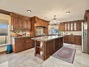 Kitchen with a center island with sink, open shelves, decorative light fixtures, freestanding refrigerator, and a chandelier