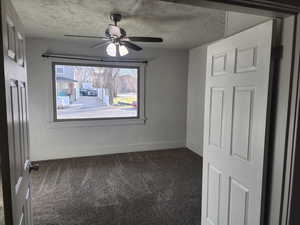 Spare room with dark colored carpet, a ceiling fan, and a textured ceiling