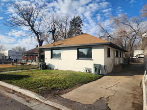 View of property exterior with brick siding, a yard, a shingled roof, and concrete driveway