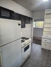 Kitchen featuring white appliances, open shelves, a textured ceiling, dark tile patterned flooring, and dark cabinetry