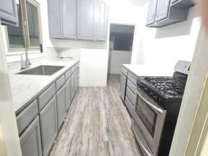Kitchen featuring gray cabinetry, gas range, light wood-style floors, and light stone counters