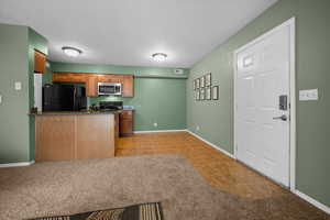 Kitchen featuring brown cabinetry, black appliances, light carpet, light tile patterned floors, and a textured ceiling
