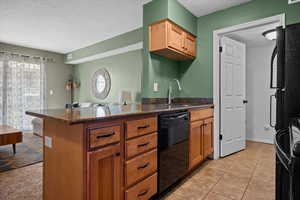 Kitchen featuring a peninsula, black appliances, a textured ceiling, brown cabinets, and dark stone countertops