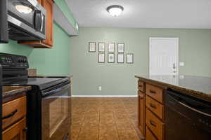 Kitchen with black appliances, brown cabinets, a textured ceiling, and dark stone countertops