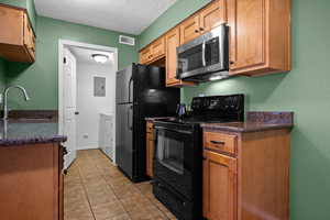 Kitchen with black appliances, brown cabinetry, light tile patterned floors, a textured wall, and a textured ceiling