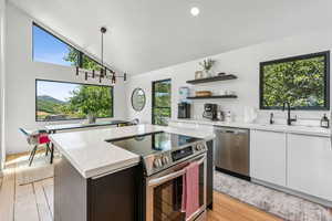 Kitchen featuring stainless steel appliances, open shelves, a center island, vaulted ceiling, and light wood-style floors