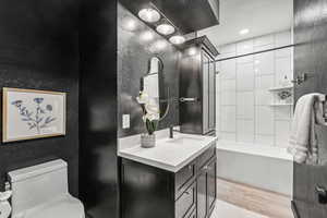 Full bath with vanity, light wood-style flooring, a textured wall, shower / tub combination, and recessed lighting