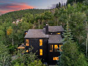 Back of property featuring a chimney, roof with shingles, and a forest view