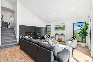 Living room featuring vaulted ceiling, light wood-style floors, a tiled fireplace, and recessed lighting