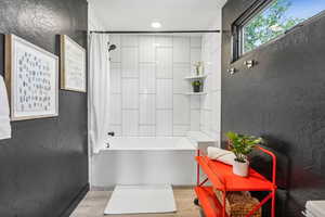 Bathroom with a textured wall, shower / bath combo, and light wood-style floors
