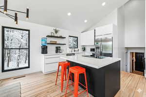 Kitchen featuring white cabinetry, stainless steel fridge with ice dispenser, a center island, open shelves, and a kitchen breakfast bar