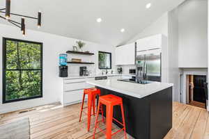 Two tone kitchen with two tone cabinetry, stainless steel fridge with ice dispenser, a kitchen island, open shelves, and lofted ceiling