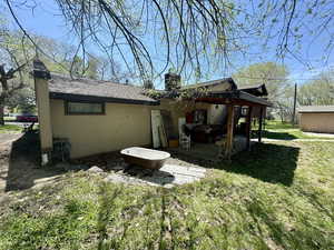Back of property featuring a chimney, stucco siding, a patio area, a shingled roof, and a lawn