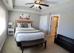 Bedroom featuring light carpet, a raised ceiling, and a ceiling fan