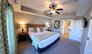 Bedroom with a tray ceiling, a ceiling fan, and carpet flooring