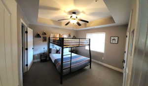 Carpeted bedroom featuring a raised ceiling and ceiling fan