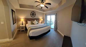 Bedroom with access to exterior, a tray ceiling, and a ceiling fan