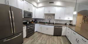 Kitchen featuring appliances with stainless steel finishes, white cabinets, pendant lighting, light wood-style flooring, and dark stone countertops