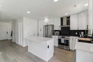 Kitchen with stainless steel appliances, white cabinets, light stone counters, a center island, and light wood-type flooring