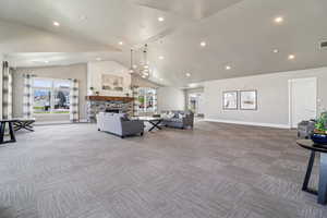 Carpeted living room with a high ceiling, a stone fireplace, and suspended lighting