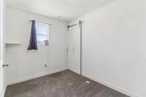 Unfurnished bedroom featuring a barn door and dark carpet