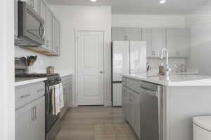 Kitchen featuring gray cabinets, stainless steel appliances, dark wood-type flooring, an island with sink, and light stone counters