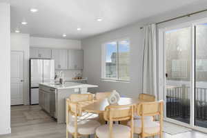 Kitchen with gray cabinetry, freestanding refrigerator, a kitchen island with sink, light wood-type flooring, and recessed lighting