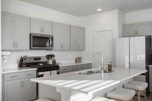 Kitchen featuring gray cabinets, stainless steel microwave, a breakfast bar, an island with sink, and freestanding refrigerator