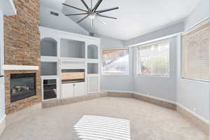 Unfurnished living room featuring built in shelves, a stone fireplace, ceiling fan, carpet floors, and lofted ceiling