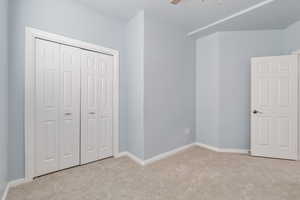 Unfurnished bedroom with light colored carpet, a closet, and a ceiling fan