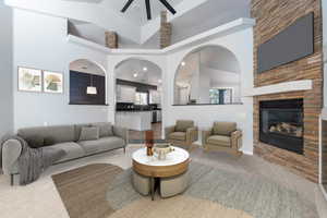 Living area with carpet, a high ceiling, a stone fireplace, and a ceiling fan