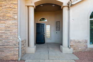 Doorway to property featuring stone siding, covered porch, and stucco siding