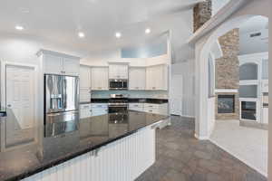 Kitchen featuring built in shelves, appliances with stainless steel finishes, dark stone countertops, dark stone finish floors, and a stone fireplace