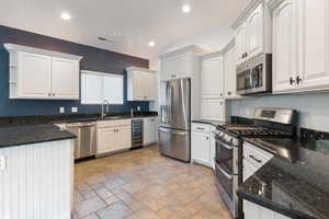 Kitchen featuring dark stone counters, appliances with stainless steel finishes, white cabinets, open shelves, and recessed lighting