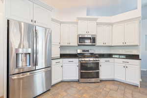 Kitchen with appliances with stainless steel finishes, stone finish flooring, dark stone countertops, and white cabinets