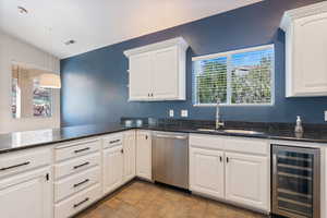 Kitchen featuring dark stone counters, wine cooler, stainless steel dishwasher, white cabinets, and stone finish floors