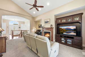Living room featuring a premium fireplace, arched walkways, light carpet, high vaulted ceiling, and a ceiling fan