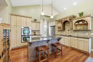Kitchen with an island with sink, stainless steel appliances, a kitchen bar, hanging light fixtures, and dark stone counters