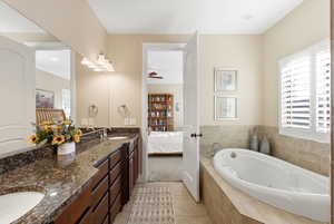 Ensuite bathroom with a whirlpool tub, double vanity, light tile patterned flooring, and a ceiling fan