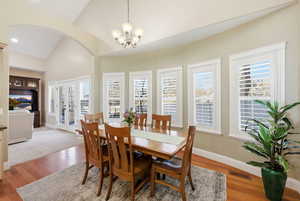 Dining room with arched walkways, french doors, a chandelier, wood finished floors, and high vaulted ceiling
