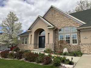 View of front of home with stone siding, stucco siding, and roof with shingles