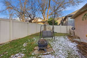 Yard layered in snow with a fenced backyard and an outdoor fire pit