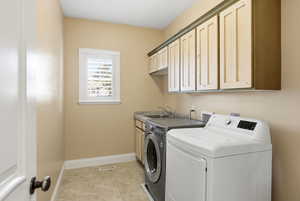 Washroom featuring cabinet space, washing machine and dryer, and light tile patterned floors