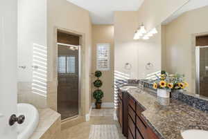 Bathroom featuring a shower stall, double vanity, a bath, and light tile patterned floors