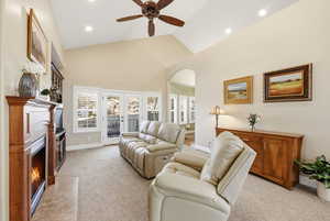 Living room with a fireplace with flush hearth, light carpet, arched walkways, french doors, and high vaulted ceiling