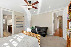 Bedroom featuring arched walkways, light colored carpet, ornamental molding, connected bathroom, and ceiling fan